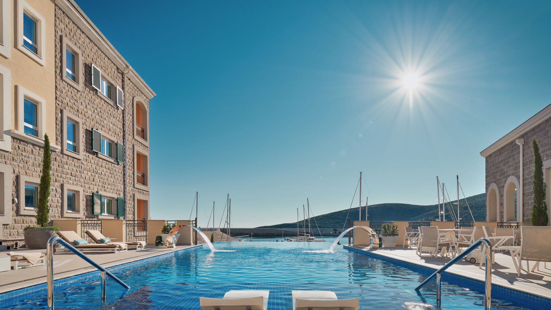 A Swimming Pool With A Building And Boats In The Background