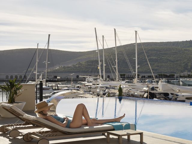A Person Lying On A Lounge Chair By A Pool With Boats In The Background
