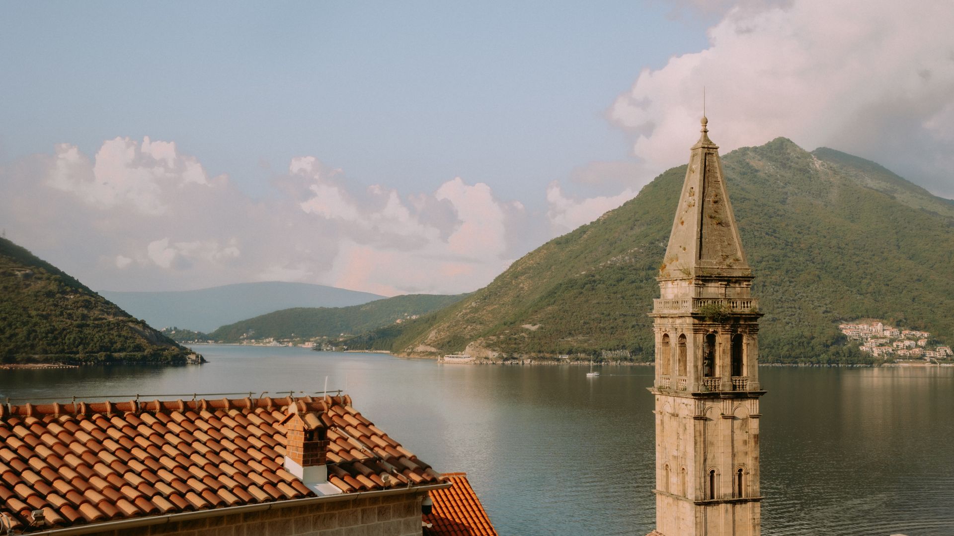 A Building With A Tower By A Body Of Water With Mountains In The Background